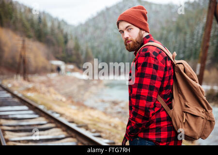 Beau jeune homme barbu en chemise à carreaux sur le chemin de fer dans les montagnes Banque D'Images