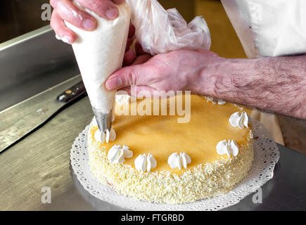 Crème tuyauterie Baker décorations sur en haut d'un gâteau à l'aide d'un gicleur et sac, Close up de ses mains et le gâteau Banque D'Images