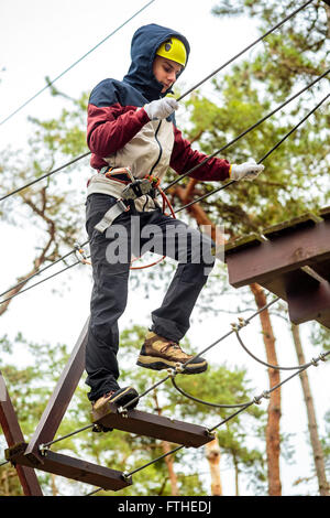 Adolescent sur un cours à un parc d'aventure avec des protections Banque D'Images