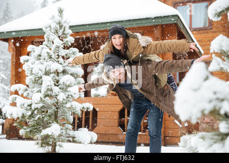 Cheerful attractive bearded man piggibacking sa petite amie et s'amuser en hiver Banque D'Images