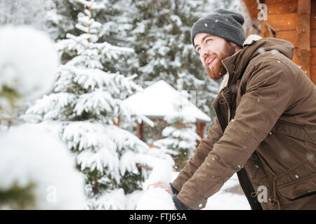 Heureux jeune homme barbu debout et bénéficiant d'un temps neigeux sur station de sports d'hiver Banque D'Images