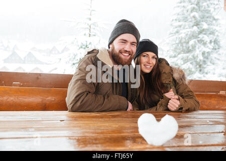 Portrait de beau jeune couple assis en plein air avec cœur fait de la neige en hiver Banque D'Images