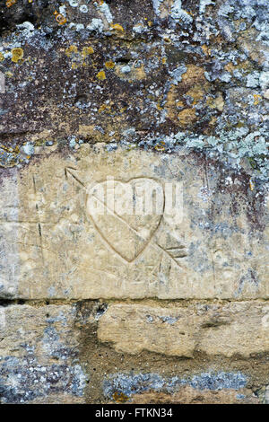 Amour coeur sculpté sur un mur en pierre de Cotswold. Bibury, Gloucestershire, Angleterre Banque D'Images