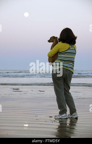 Femme avec chien dans lap en admirant la plage full moon - Bertioga - côte nord de SP Banque D'Images