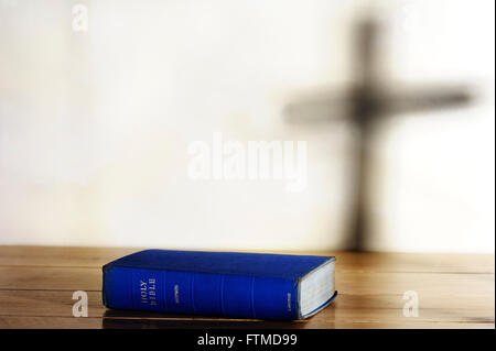 Ancienne copie de la Sainte Bible allongé sur une table avec l'ombre d'une croix sur l'arrière-plan. Banque D'Images