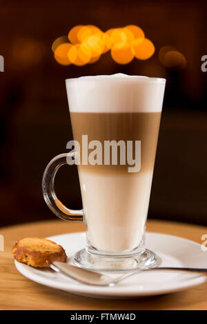 Caffe café macchiato boisson dans un verre, servi dans un café sur une soucoupe d'un biscuit. Banque D'Images