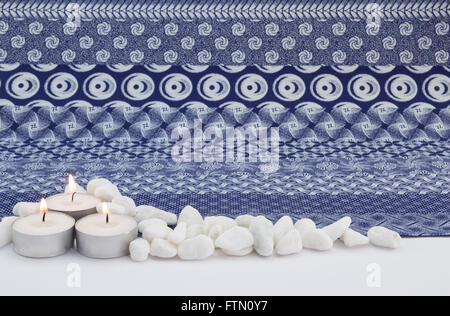 Close up de trois petits allumé des bougies blanches avec des cailloux blancs et fond en tissu imprimé indigo Banque D'Images