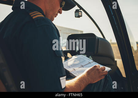 Pilote d'hélicoptère de l'homme lire un manuel brochure tout en restant assis dans le cockpit. Banque D'Images