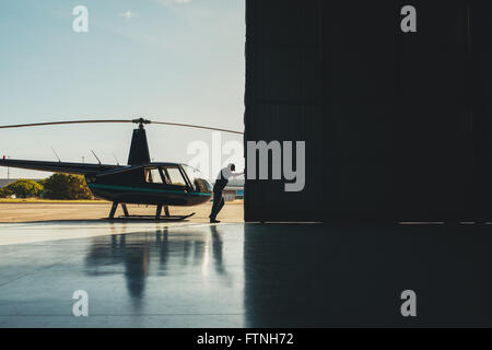 Poussant la porte de mécanicien d'un hangar avec un hélicoptère. L'ouverture de l'hélicoptère Pilote porte du hangar. Banque D'Images