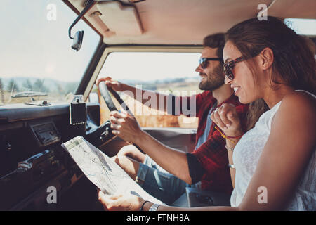 Vue latérale du jeune couple à l'aide d'une carte sur un roadtrip pour les directions. Young man and woman reading a map tout en restant assis dans une voiture.