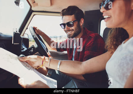 Jeune homme conduisant la voiture avec femme tenant une feuille de route. Jeune couple on road trip. Banque D'Images