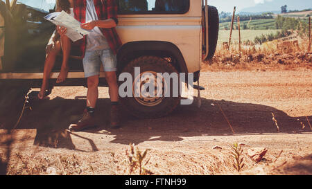 Cropped shot of couple avec une carte on road trip. Jeune homme et femme avec l'arrêt de voiture par une route de campagne et la lecture de carte pour dire Banque D'Images