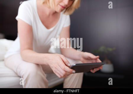 Cropped shot of a woman using digital tablet, assis sur le bord du lit. L'accent sur tablet pc et femme mains. Banque D'Images
