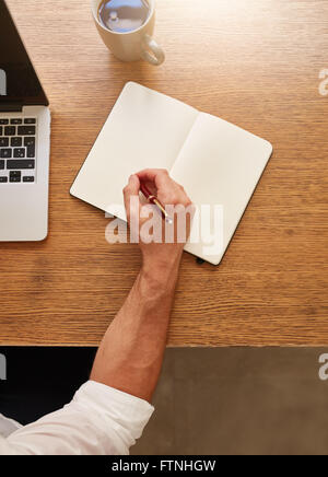 Vue de dessus de l'homme tourné en quelques notes dans son journal tout en restant assis à sa place de travail. Banque D'Images