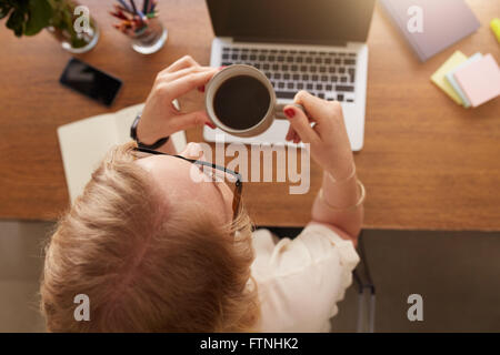 Vue de dessus de femme à boire du café alors qu'assise à son bureau au bureau à domicile. Banque D'Images