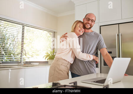 Tourné à l'intérieur du couple amoureux en cuisine avec un ordinateur portable. L'homme et la femme mature enlacés et souriant avec un ordinateur portable sur ki Banque D'Images