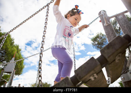 Belle petite fille escalade un petit pont en bois sur l'aire de jeux Banque D'Images