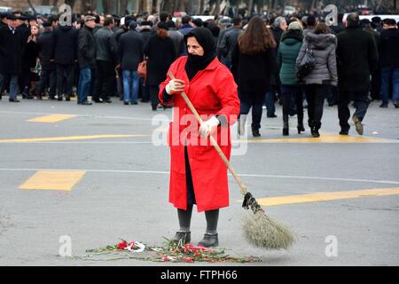 BAKU, AZERBAÏDJAN - le 20 janvier 2014 Femme au manteau rouge balayer jusqu'œillets rouges Banque D'Images