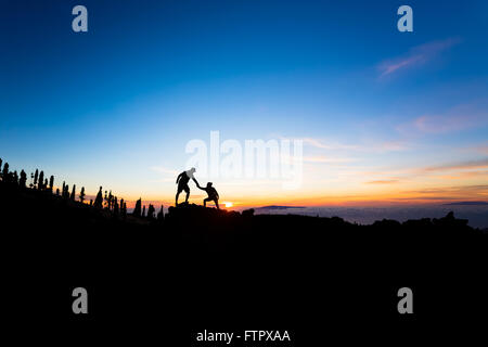 Couple d'équipe aide aide confiance silhouette dans les montagnes, le coucher du soleil. Équipe d'alpinistes l'homme et la femme les randonneurs, aider les uns les autres Banque D'Images