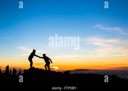 Couple d'équipe aide aide confiance silhouette dans les montagnes, le coucher du soleil. Équipe d'alpinistes l'homme et la femme les randonneurs, aider les uns les autres Banque D'Images