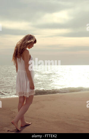 Blonde woman walking on beach looking down Banque D'Images