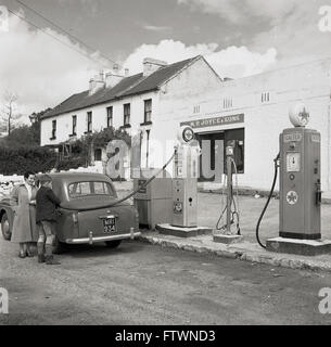 Années 1950, historique, dans une station-service rurale/garage dans l'ouest de l'Irlande, un jeune lad remplit une voiture de dame, peut-être un Austin de style britannique, avec du carburant. Banque D'Images