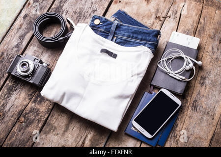 Femme voyageant de trucs sur fond de bois. Smartphone avec écran noir et des vêtements avec caméra disposées sur le bureau Banque D'Images