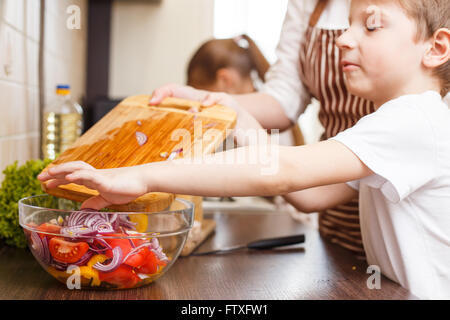 Arrière-plan de cuisine familiale. Petit garçon aider sa mère avec salade de mélange dans la cuisine Banque D'Images