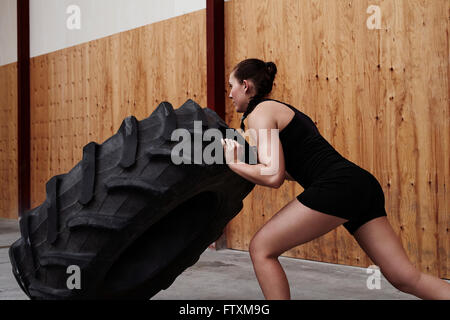 Jeune femme poussant dans la salle de sport des pneus de camion Banque D'Images