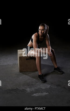 Jeune femme assise sur un coffret en bois dans une salle de sport Banque D'Images