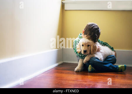 Garçon assis sur le sol, serrant chiot golden retriever dog Banque D'Images