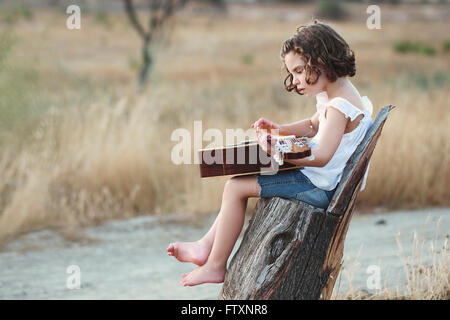 Fille assise dans un champ à jouer de la guitare Banque D'Images