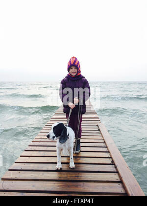 Fille et son chien debout sur la jetée par la mer Banque D'Images