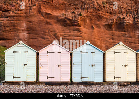 Beach Hut ligne dans des couleurs pastel, red rock fond, dans le sud du Devon, UK Banque D'Images