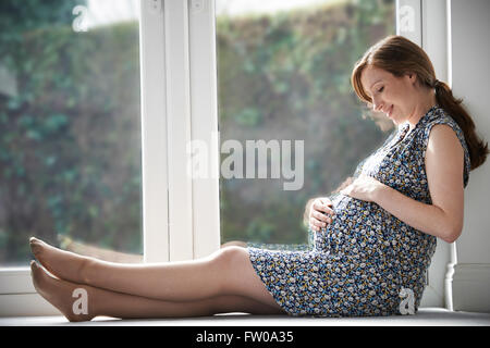 Femme enceinte en relaxant à la maison de la fenêtre Banque D'Images