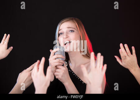 Portrait de belle fille passionnés chantant holding silver vintage microphone, foule des mains du ventilateur sur le premier plan Banque D'Images