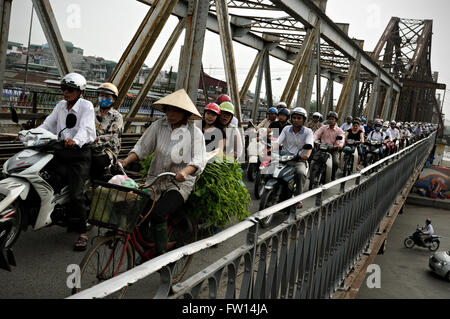 Woman riding a bicycle et beaucoup d'autres personnes la trottinette, le pont Long Bien à l'heure de pointe à Hanoi, Vietnam Banque D'Images