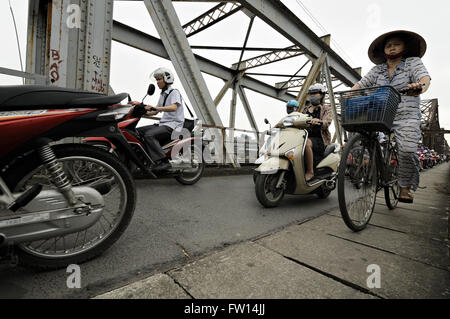 Femme au chapeau conique typique d'une bicyclette et beaucoup d'autres personnes la trottinette, le pont Long Bien à Hanoi, Vietnam Banque D'Images