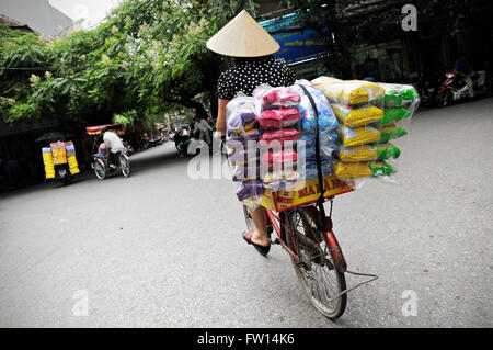 Femme avec un chapeau conique typique de transport de marchandises sur son vélo à Hanoi, Vietnam Banque D'Images