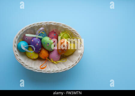 Panier tissé blanc avec sélection d'oeufs de Pâques colorés avec des rubans isolé sur fond bleu Banque D'Images