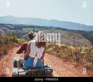 Vue arrière shot of young couple riding sur un quad en campagne. Femme derrière son petit ami la conduite d'un VTT sur les routes de campagne, o Banque D'Images