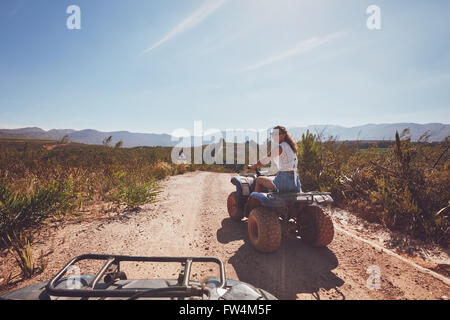 Jeune femme au volant d'un quad sur route de campagne. Jeune femme sur un véhicule tout terrain dans la nature sur une journée ensoleillée. Banque D'Images