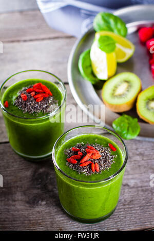 Smoothie vert frais saupoudrés de graines de chia et les baies de goji dans l'arrière-plan les fruits et légumes sur la table en bois. Banque D'Images