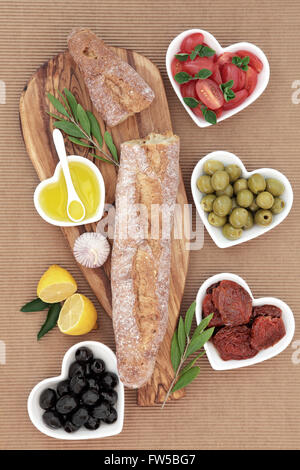 Baguette de pain français sur une carte en bois d'olivier avec des produits frais et des tomates séchées, olives vertes et noires et l'huile en forme du cœur b Banque D'Images