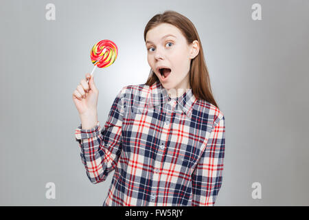 Assez étonné adolescente en chemise à carreaux avec bouche ouverte holding lollipop Banque D'Images