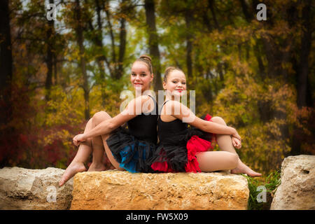 Deux soeurs poser dos à dos en tutus de ballet sur un rocher dans le parc en automne Banque D'Images