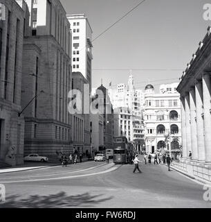 Années 1950, photo historique, scène de rue dans le centre de Hong Kong, dans le quartier financier, montrant de grands immeubles de bureaux, une grande rue avec des tramways et des lignes de tramway au milieu de la route. Banque D'Images