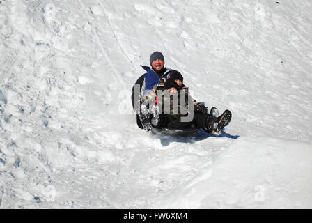 Son père et ses deux boys sledding down un snowhill en riant et s'amusant. Banque D'Images