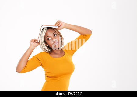 Funny pensive young african american woman with livre sur sa tête sur fond blanc Banque D'Images