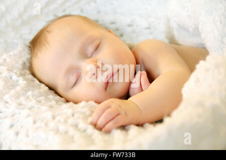 Un doux nouveau-né fille, c'est dormir paisiblement pendant que se blottit dans des couvertures blanches Banque D'Images